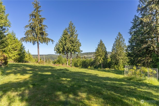 Looking NW across the lot. Neighbors have limbed trees to preserve the view. There is a dead tree that looks like a bare pole below the limbs of the left tall tree. A white boundary marker at the base of that pole defines the farthest corner of this lot and the one below.