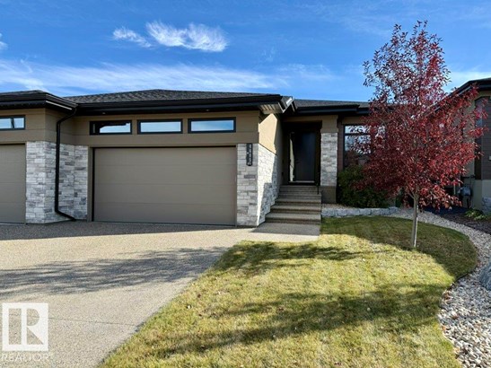 Prairie-style home featuring stone siding, a front yard, driveway, and stucco siding