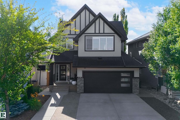 View of front of home featuring stone siding, concrete driveway, an attached garage, and roof with shingles
